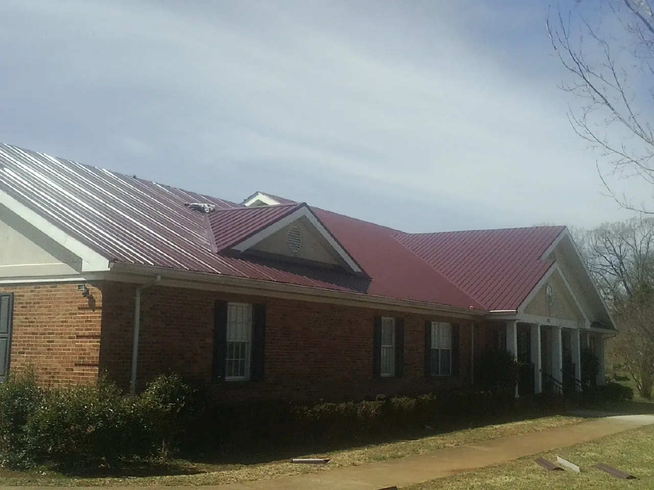 Red metal roof with gabled entries on a long brick building, from a Hail Damage Roof Repair job in Bolinas