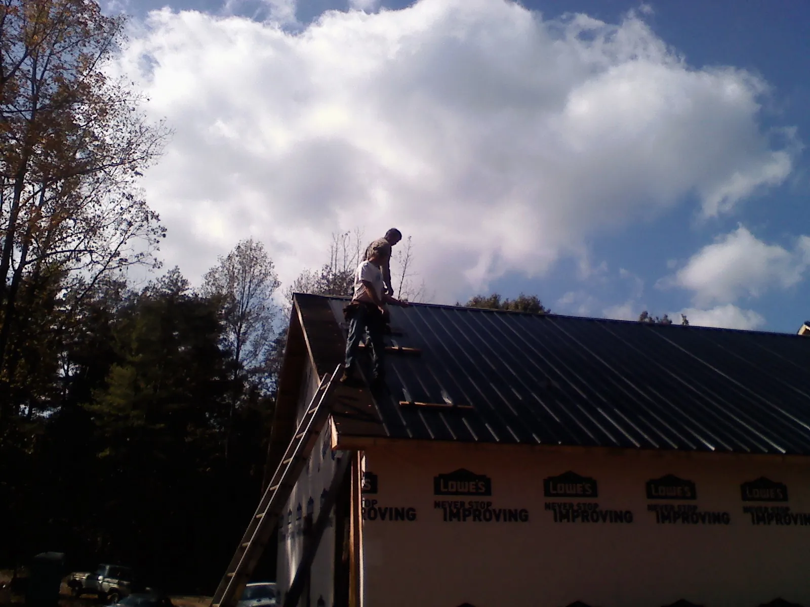 Roofer fastening dark metal panels high against a cloudy sky, from a Roof Inspection job in Bolinas