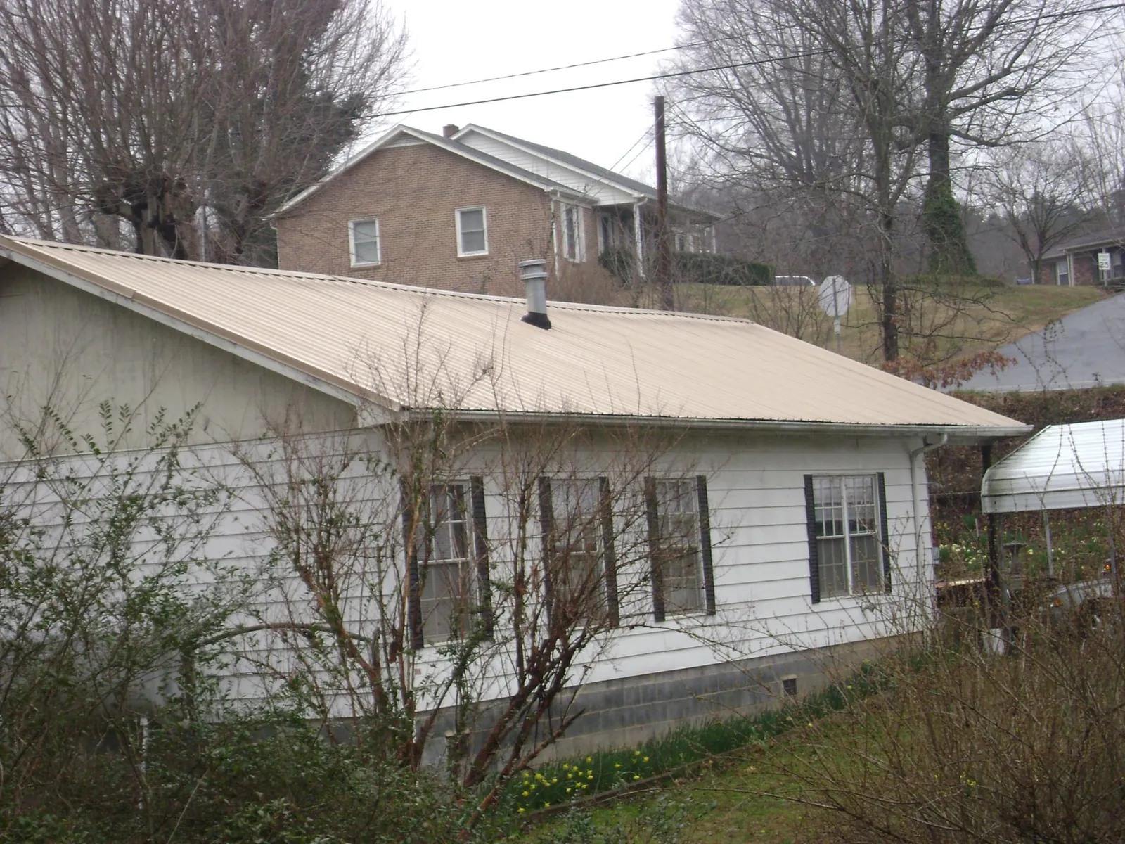 Tan metal roof on a white sided house set into a hillside — Commercial Roofing by Roofing Brothers in Bolinas